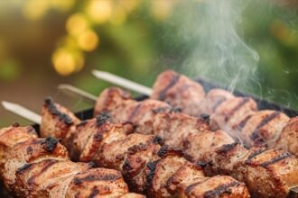 Saftige Schaschlik-Spieße grillen auf einem Mangal über glühender Holzkohle im Garten