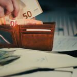 Hand placing euro banknotes into a brown leather wallet.