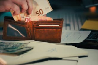 Hand placing euro banknotes into a brown leather wallet.